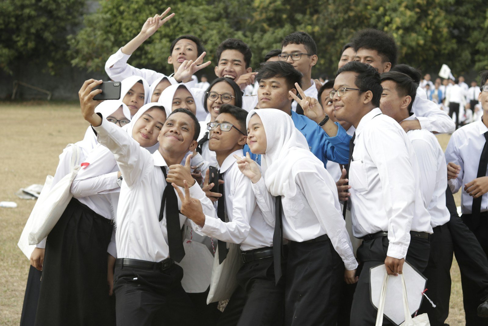 A crowd of Southeast Asian high school students in white uniforms squeezing together for a group selfie at a school gathering — the kind of new-student intake a school handles each enrollment season
